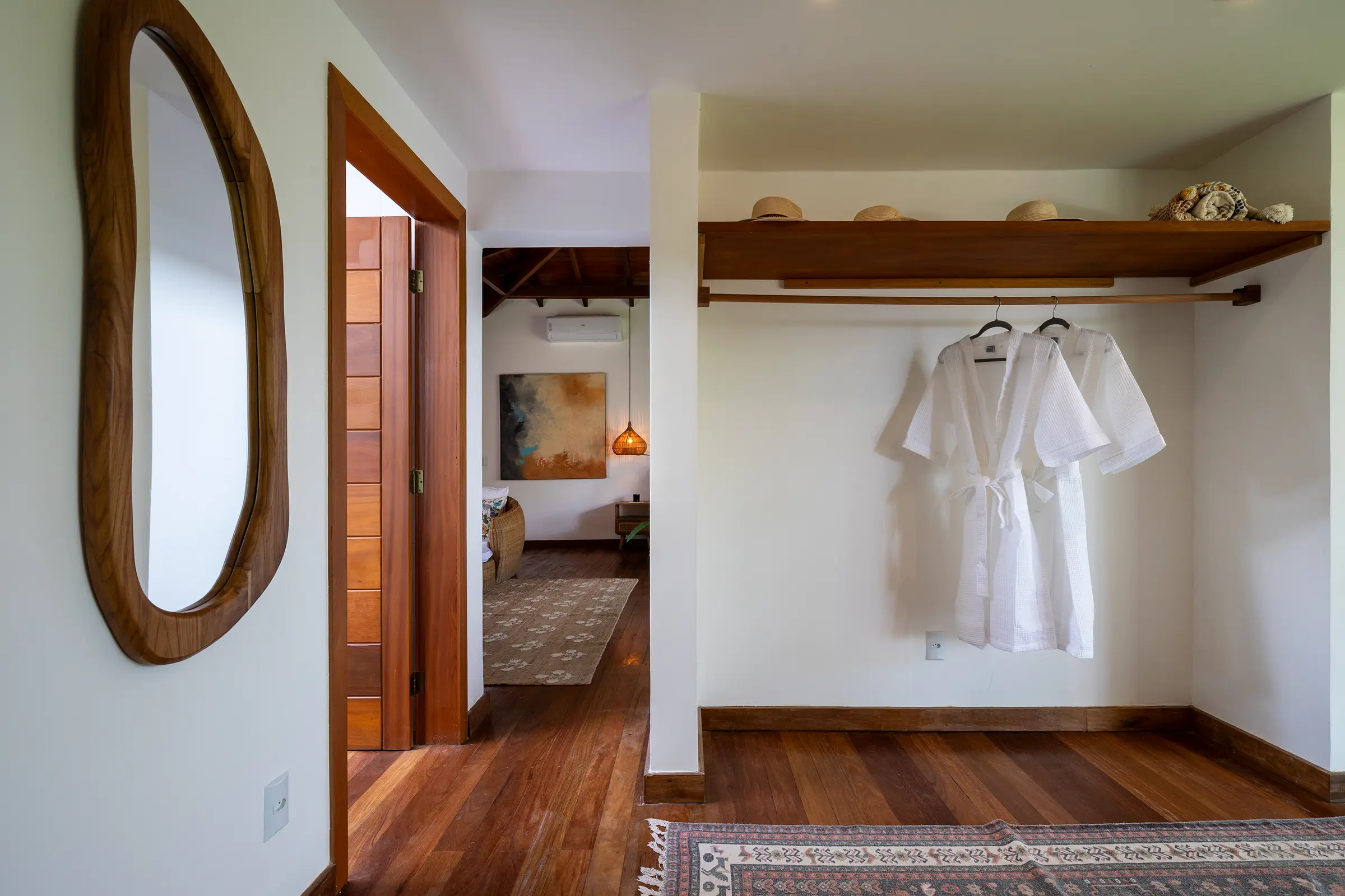 Closet com espelho de madeira orgânica e roupões, com vista para o quarto