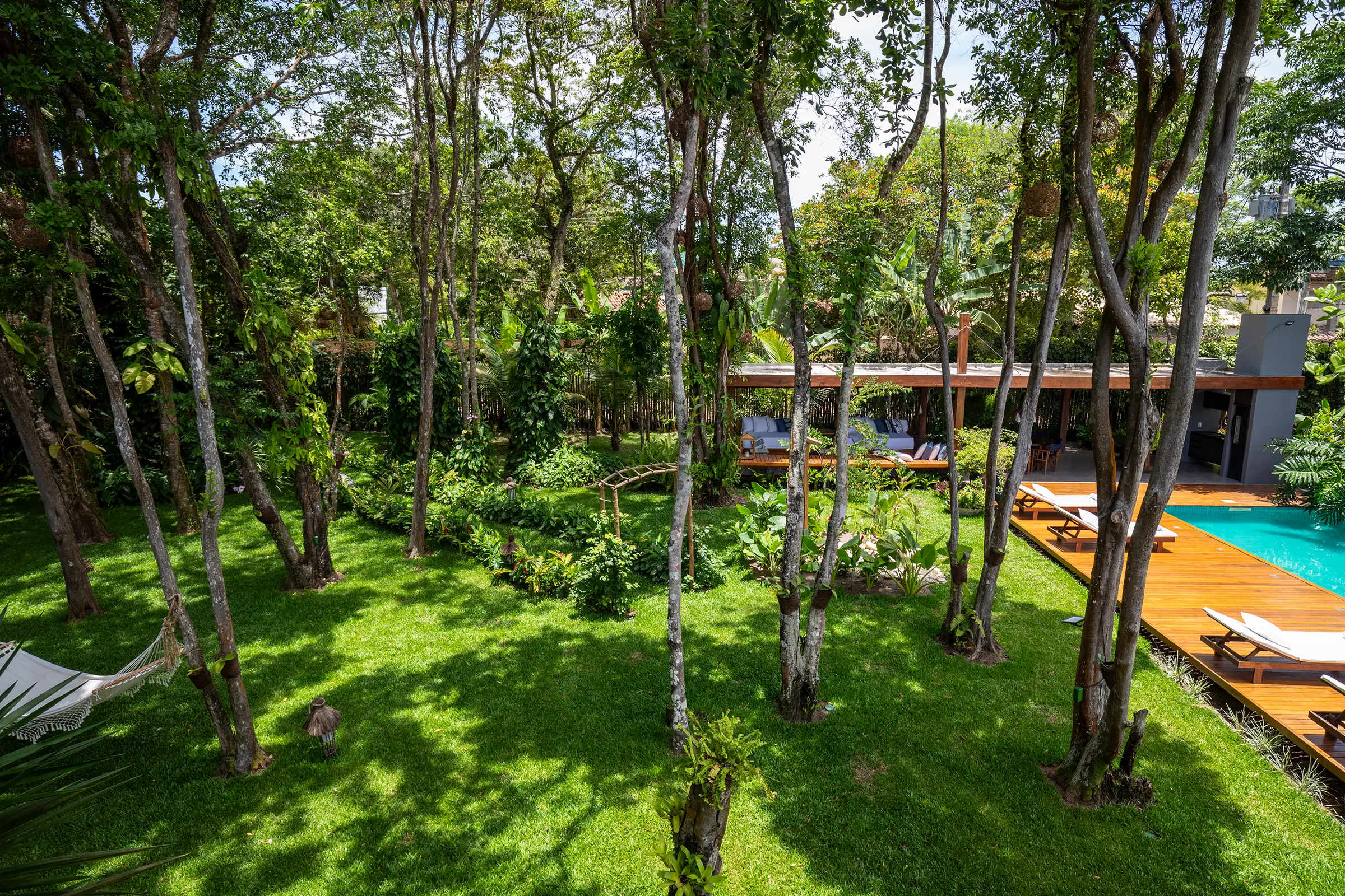 Jardim visto de cima, com rede, pavilhão e deck sob sol forte