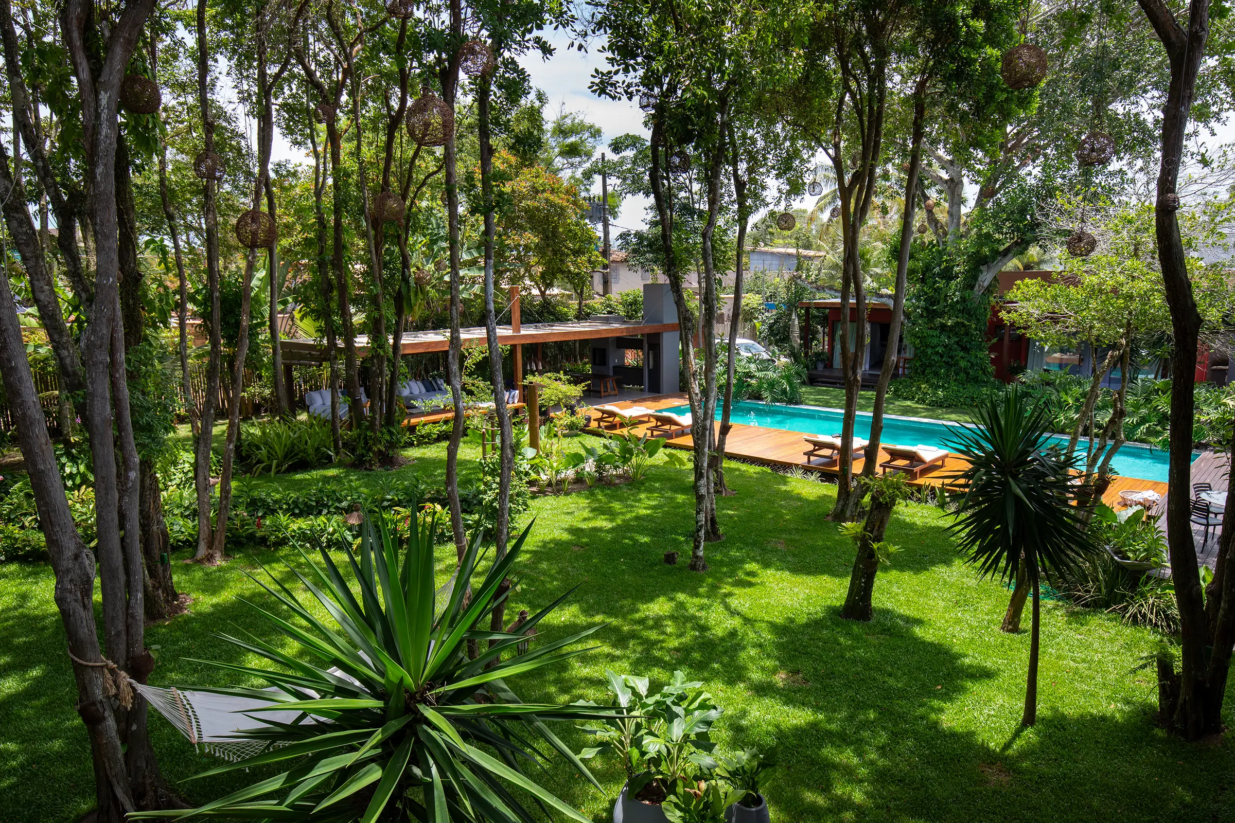 Jardim com iúca, rede e a faixa turquesa da piscina ao fundo
