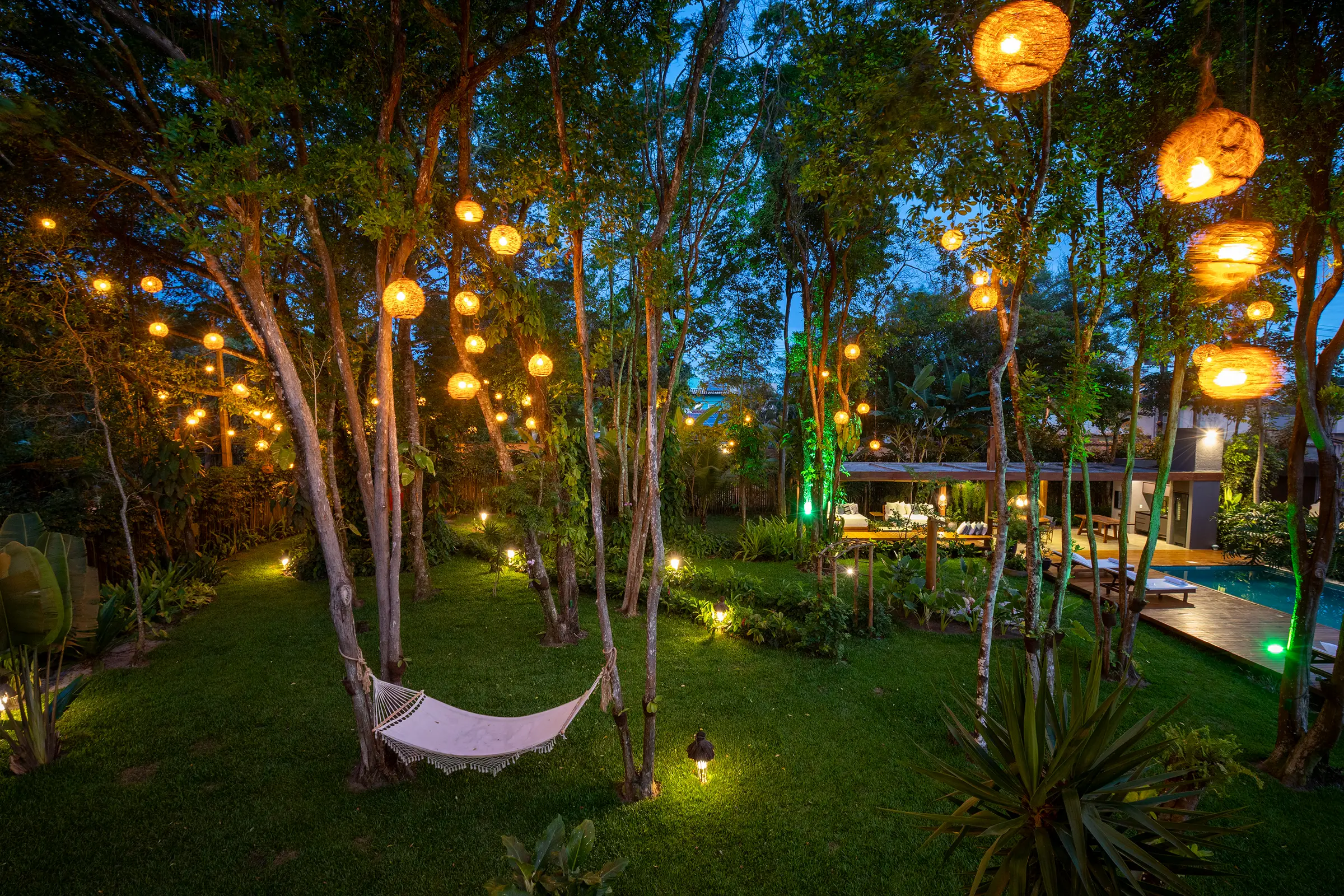 Rede entre dezenas de lanternas tecidas, com a piscina e o pavilhão à direita, à noite