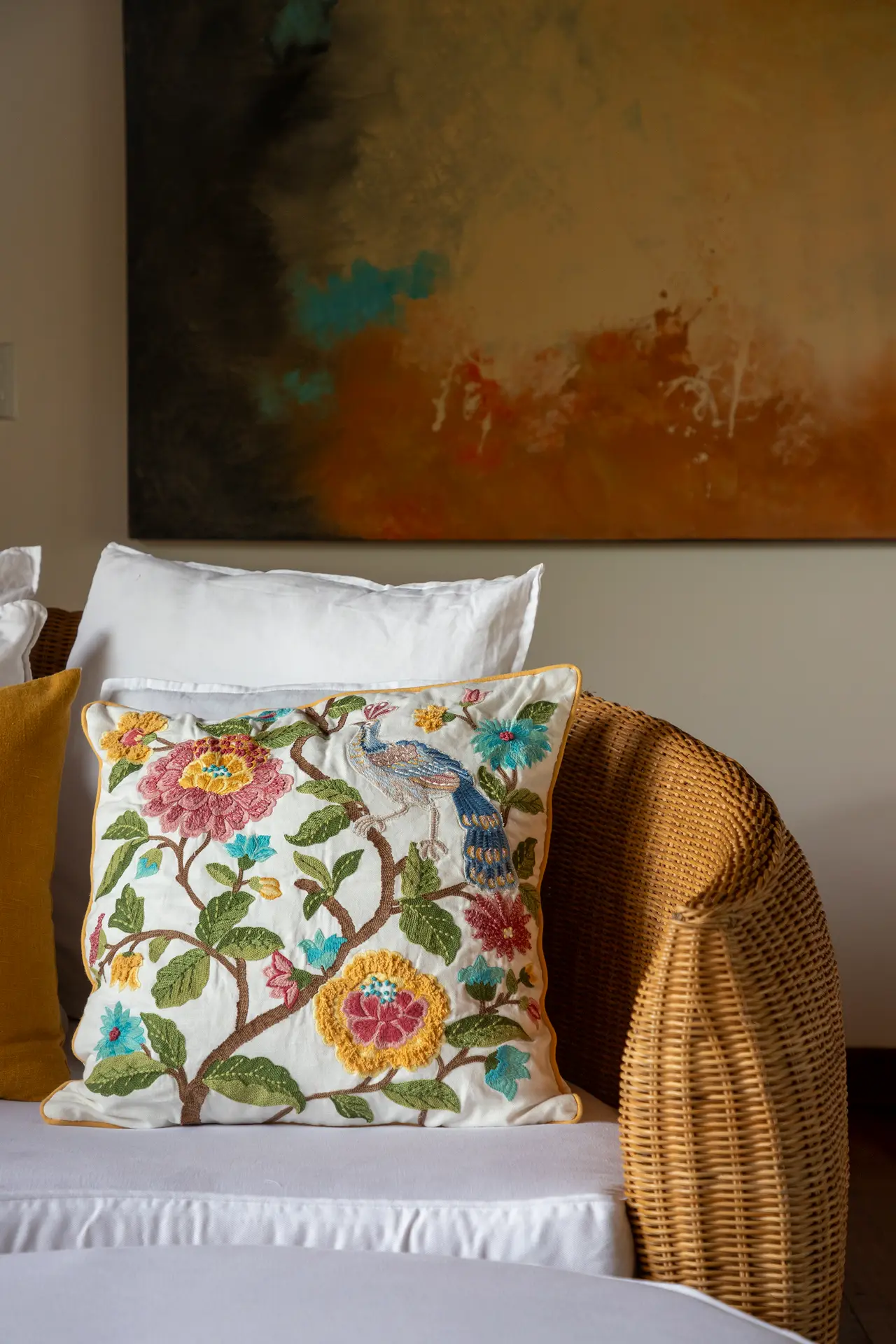 Almofada bordada com pavão sobre um daybed de vime, diante de uma pintura terracota