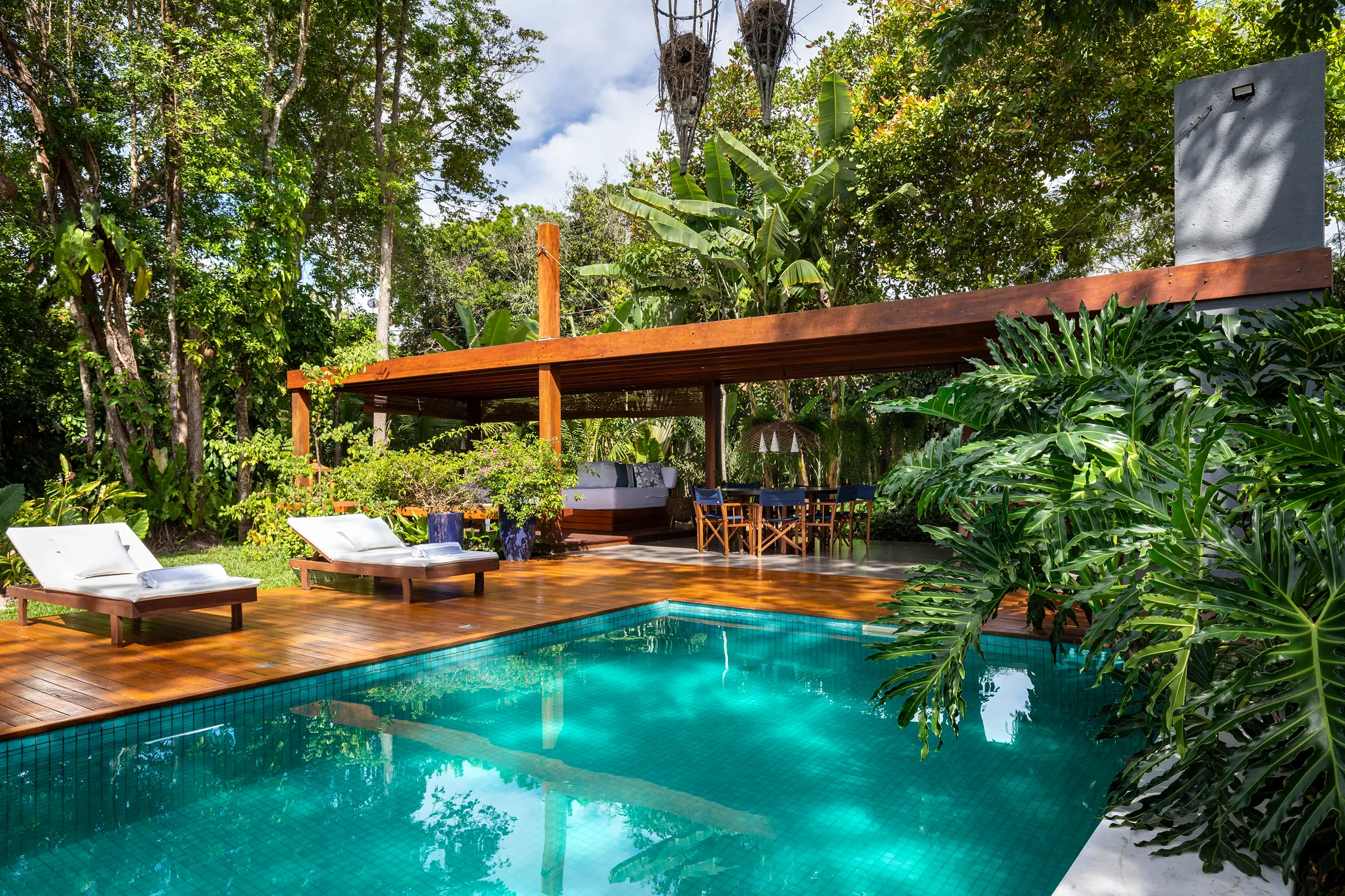 Canto da piscina com o pavilhão, luminárias de palha penduradas e folhas de bananeira