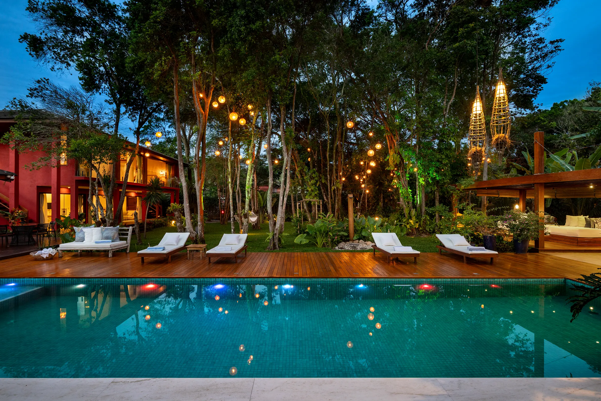 Vista frontal da piscina com quatro espreguiçadeiras e jardins de lanternas suspensas