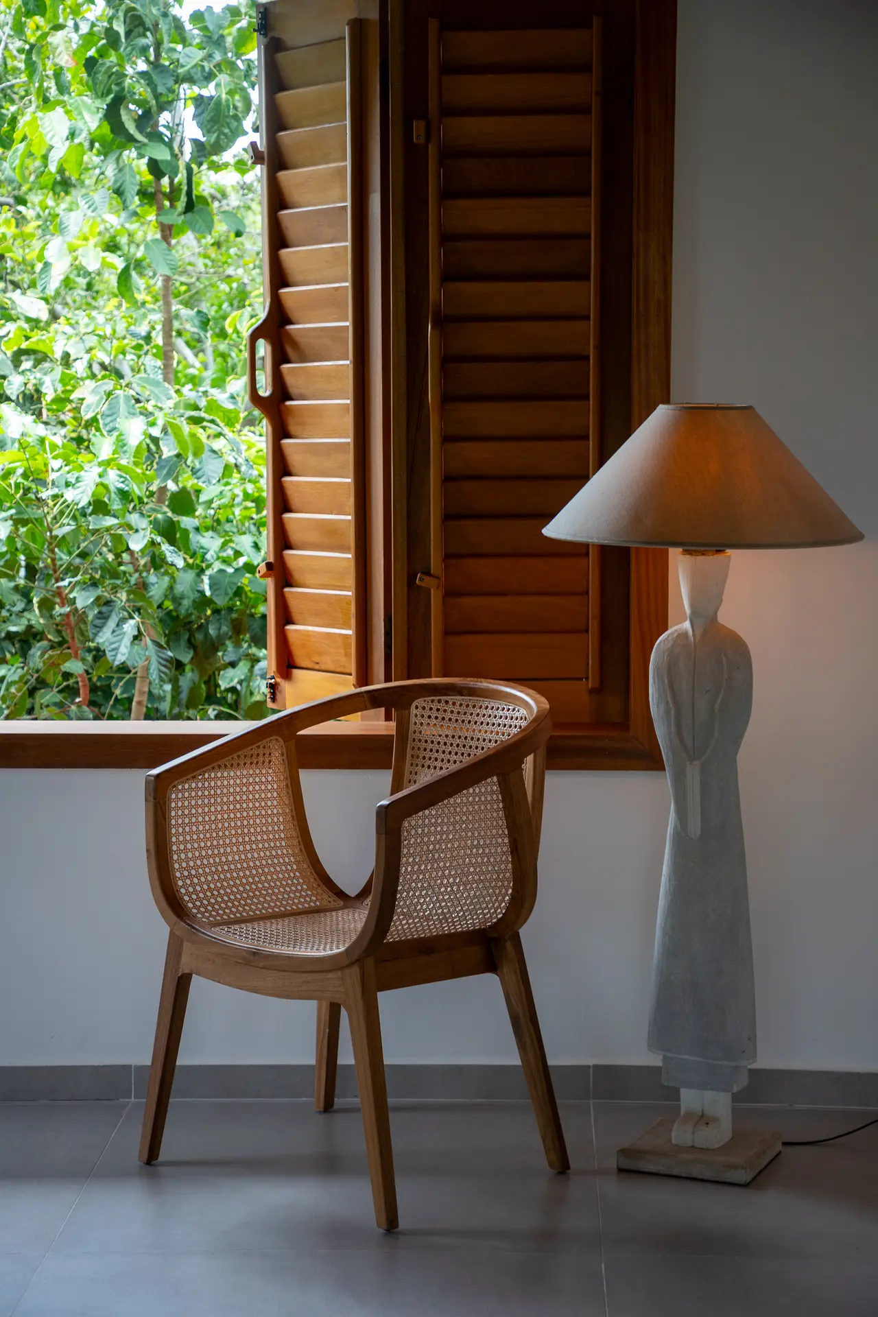 Poltrona de rattan, luminária de chão em forma de estátua e persianas de madeira